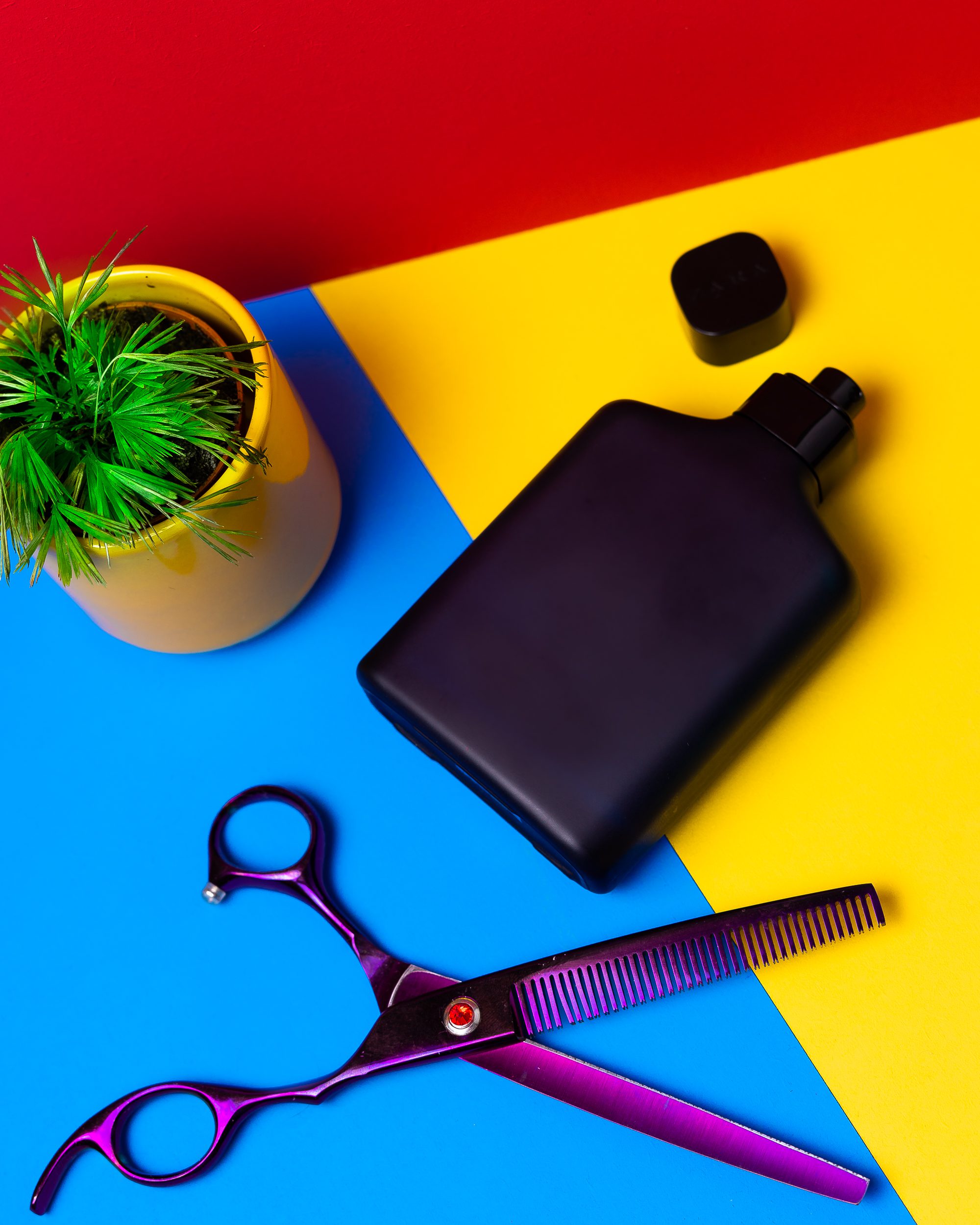 Scissors lay next to a mens perfume bottle on a primary colour background