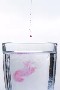Red Liquid Droplets Fall Into A Clear Glass Of Water