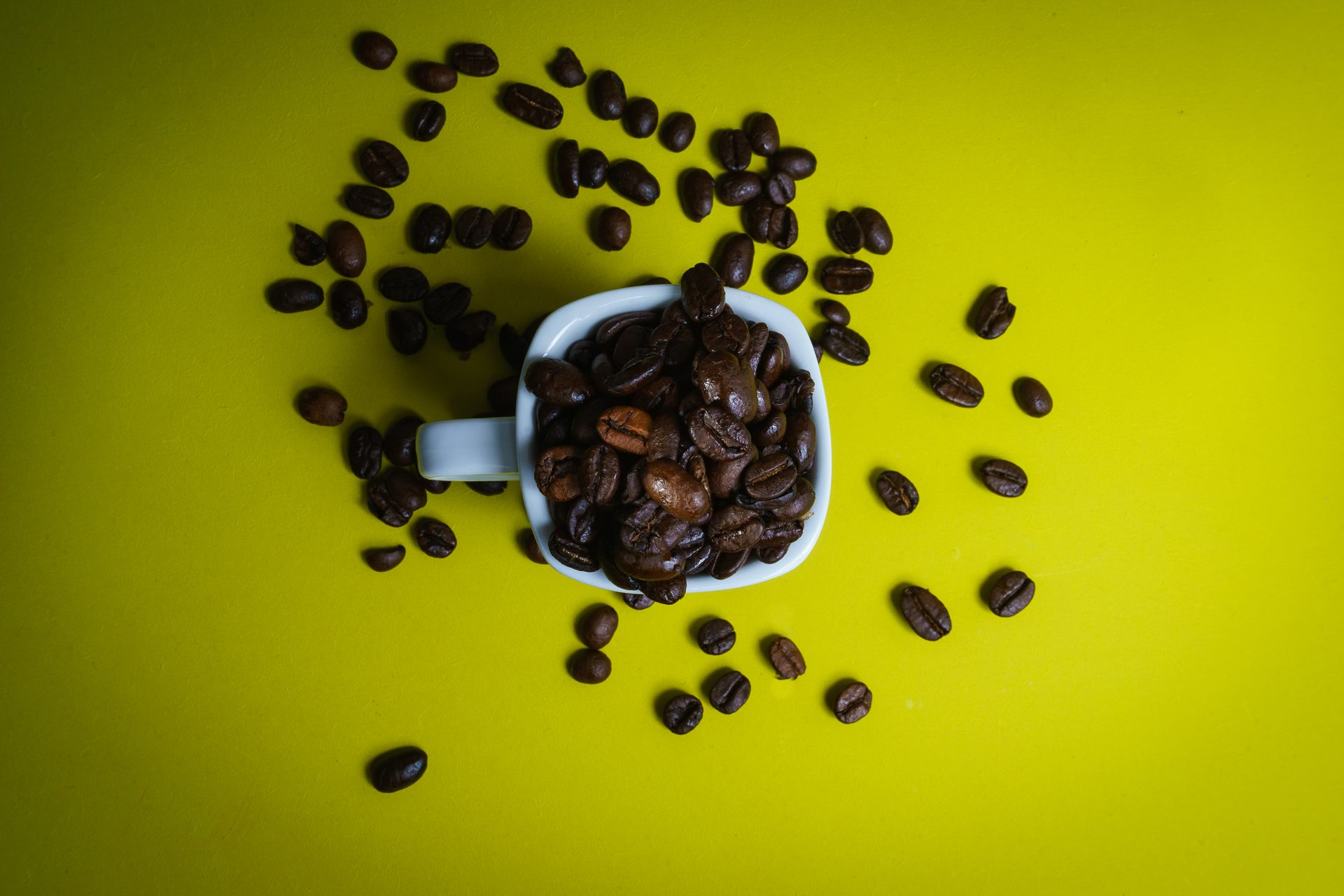 Birds Eye Of Espresso Cup Overfilled With Coffee Beans On Green Background