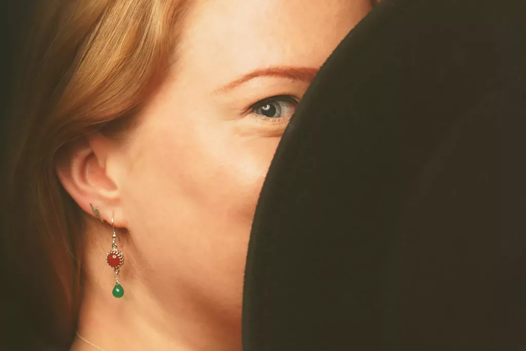 Red Stone Drop Earrings On A Woman Hiding Face Behind Black Hat